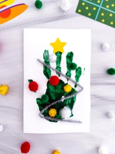 a Handprint Christmas Tree Card made with a green handprint, pipe cleaner, and pom poms