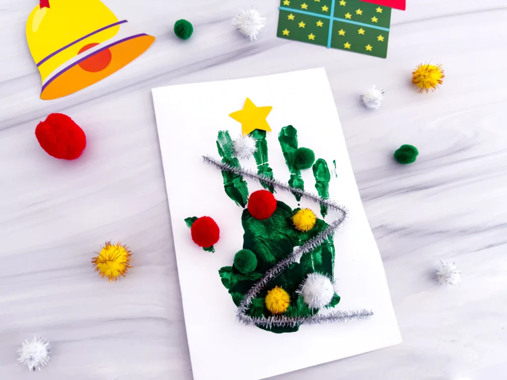 a Handprint Christmas Tree Card made with a green handprint, pipe cleaner, and pom poms