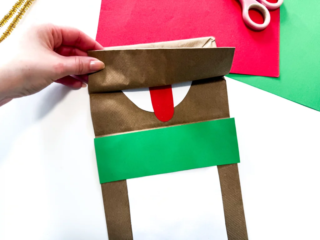 a hand opens a brown paper bag flap to show a tongue made out of construction paper