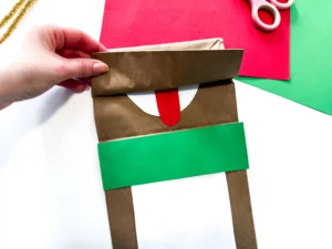 a hand opens a brown paper bag flap to show a tongue made out of construction paper