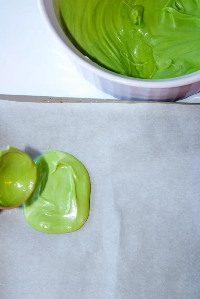 Bright green, glossy chocolate swirled inside a white bowl with some on parchment