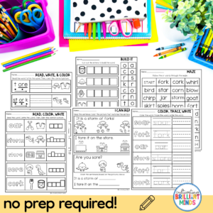 Desk with multiple black-and-white literacy worksheets (Read, Write & Color; Build It; Maze; I Can Read) and colorful school supplies.