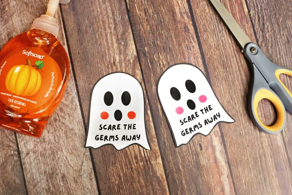 Orange Softsoap hand soap bottle on a wooden surface with three ghost-shaped tags that say'Scare the germs away' and a pair of scissors nearby.