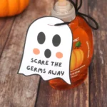 Pumpkin-themed hand soap bottle on a wooden surface with a ghost-shaped tag reading 'Scare the germs away'.