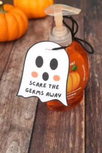 Pumpkin-themed hand soap bottle on a wooden surface with a ghost-shaped tag reading 'Scare the germs away'.
