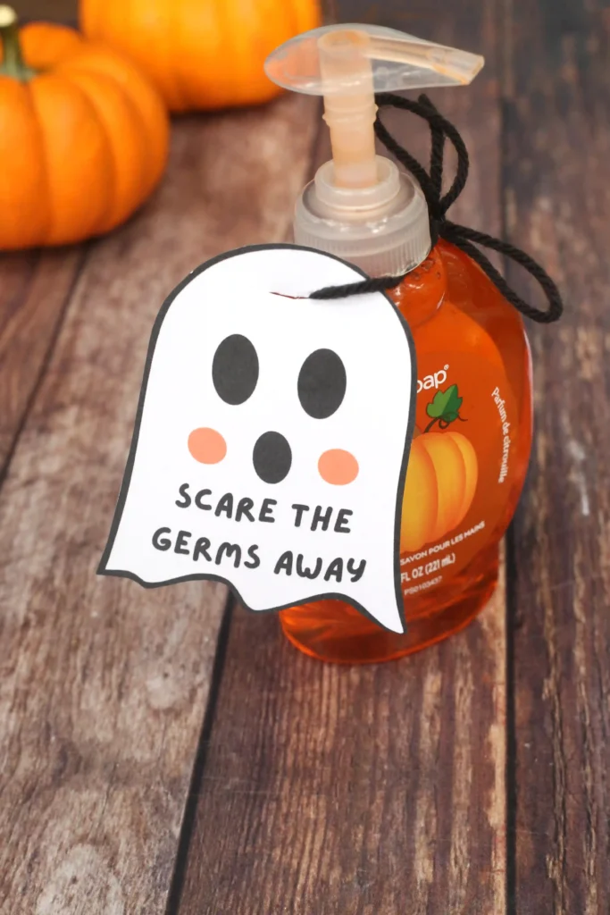 Pumpkin-themed hand soap bottle on a wooden surface with a ghost-shaped tag reading'Scare the germs away'.