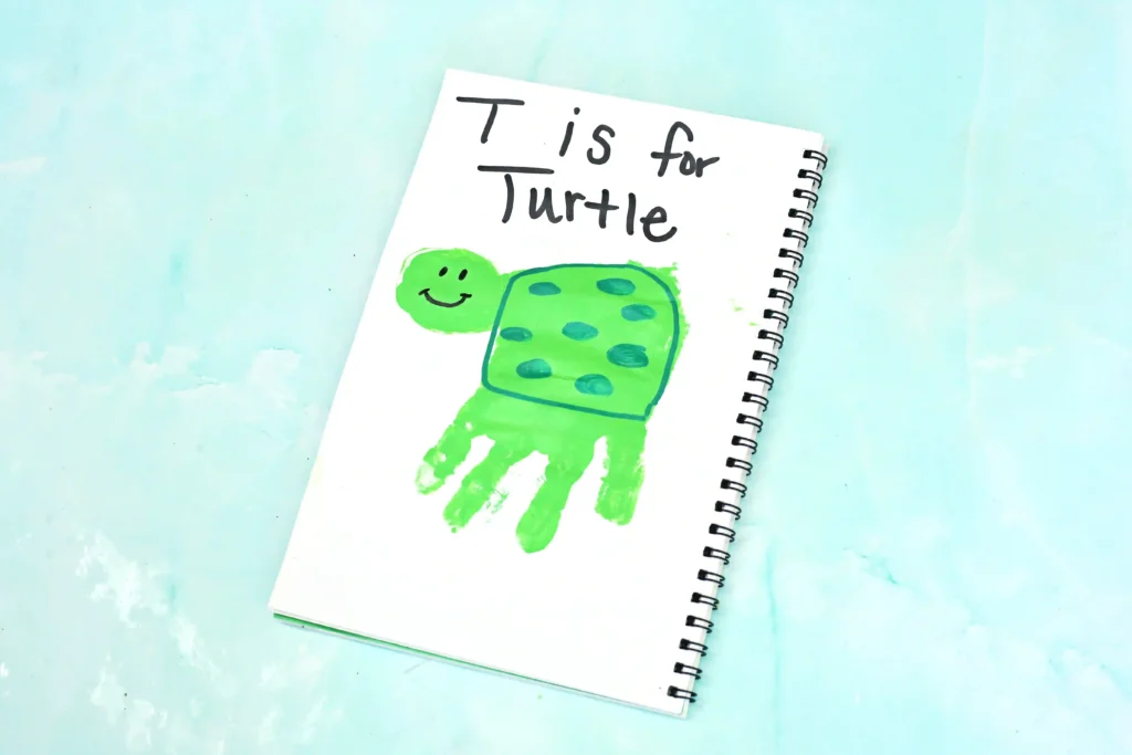 Notebook page with a green turtle drawing and the words'T is for Turtle' in black handwriting on a light blue background.