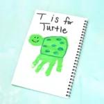 Notebook page with a green turtle drawing and the words 'T is for Turtle' in black handwriting on a light blue background.