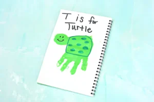 Notebook page with a green turtle drawing and the words 'T is for Turtle' in black handwriting on a light blue background.