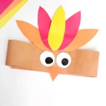 Colorful paper collage of a cartoon turkey with orange head, yellow and pink feathers, and large googly eyes on a white background.