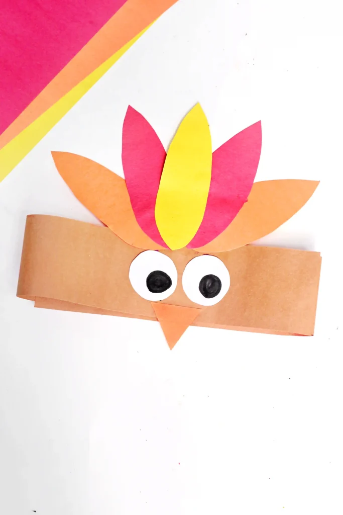 Colorful paper collage of a cartoon turkey with orange head, yellow and pink feathers, and large googly eyes on a white background.
