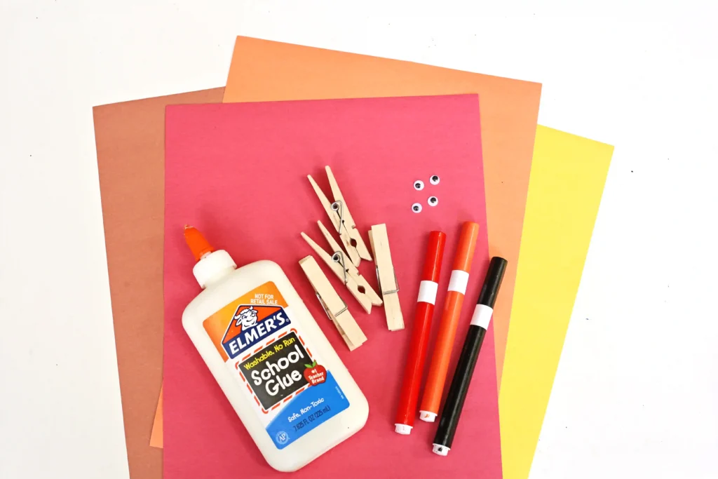 supplies for the DIY Thanksgiving Place Cards: Glue bottle, wooden clothespins, and red markers on layered colored construction papers.