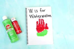 a watermelon handprint craft of a red and green handprint with watermelon seeds and words that read "w is for watermelon"