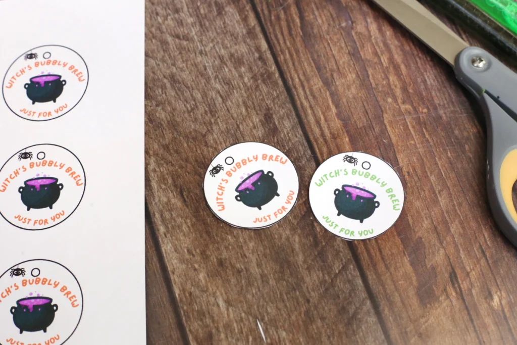 Round stickers with a bubbling purple cauldron and orange text'Witch's Bubbly Brew Just for you' on a wooden table.