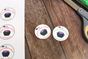 Round stickers with a bubbling purple cauldron and orange text 'Witch's Bubbly Brew Just for you' on a wooden table.