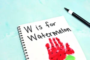 a watermelon handprint craft of a red and green handprint with watermelon seeds and words that read "w is for watermelon"