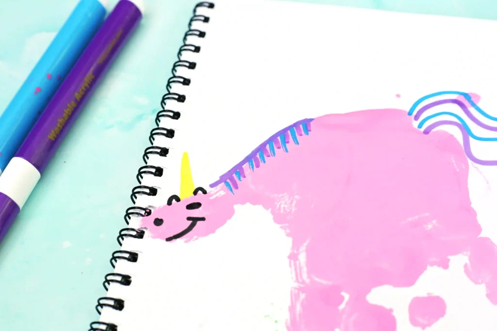 Colorful desk scene with a spiral notebook, a handprint unicorn on the page