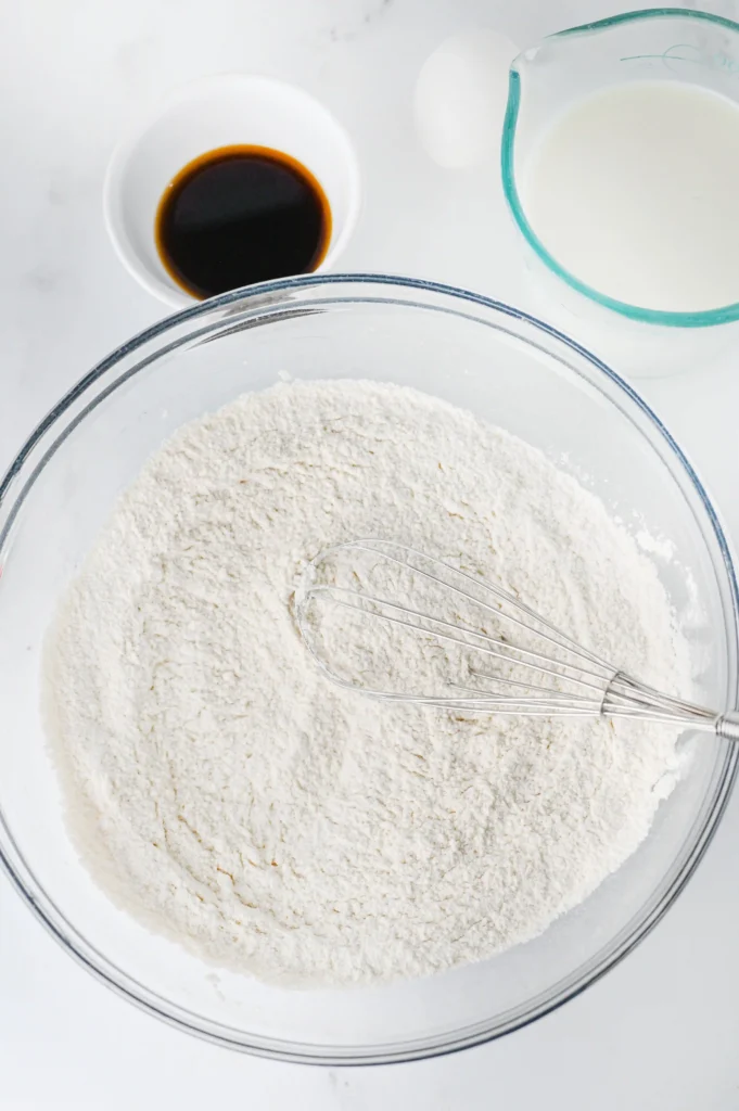 flour, sugar, baking powder, baking soda, and salt in a glass bowl with a whisk