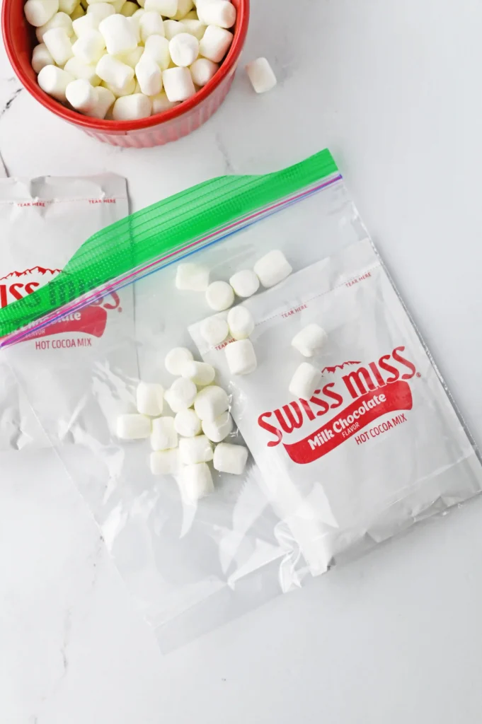 Mini white marshmallows spilling from a Swiss Miss hot cocoa mix packet onto a light marble surface.