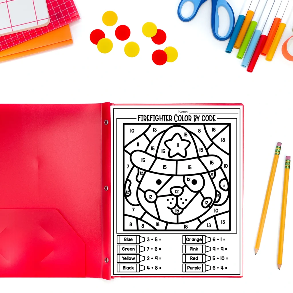 Open red binder showing a firefighter color-by-code worksheet surrounded by colored pencils, markers, scissors, and notebooks.
