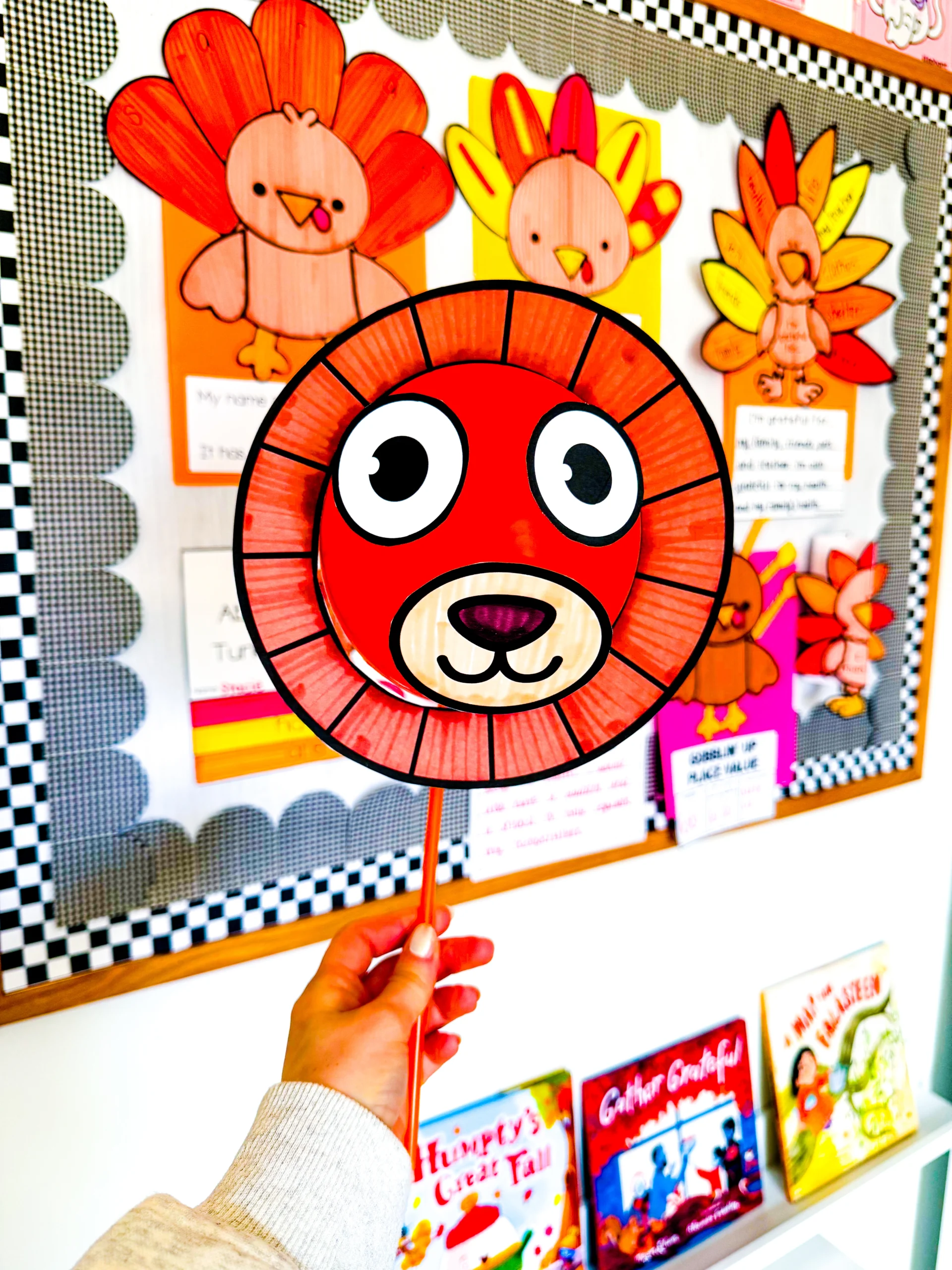 Colorful classroom display of lion-themed student artwork on orange mane held by a hand on a wand.