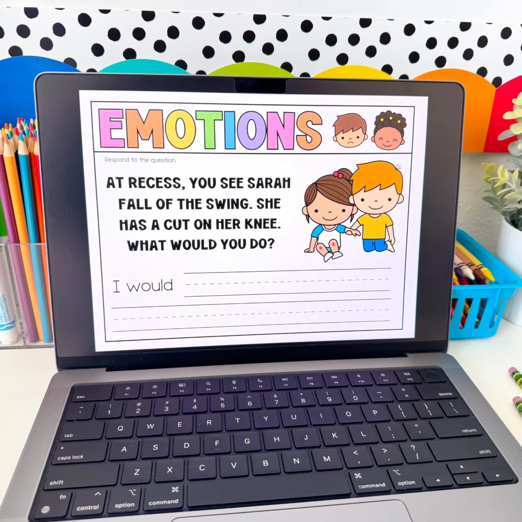 Laptop screen displaying a colorful'EMOTIONS' worksheet with cartoon kids and text about recess, placed among colored pencils and bright background dots.