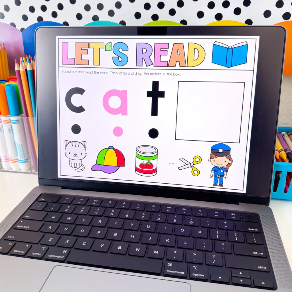Laptop screen shows a colorful'LET'S READ' banner with a blue open book icon, set on a desk with colored pencils nearby—an educational reading page setup.