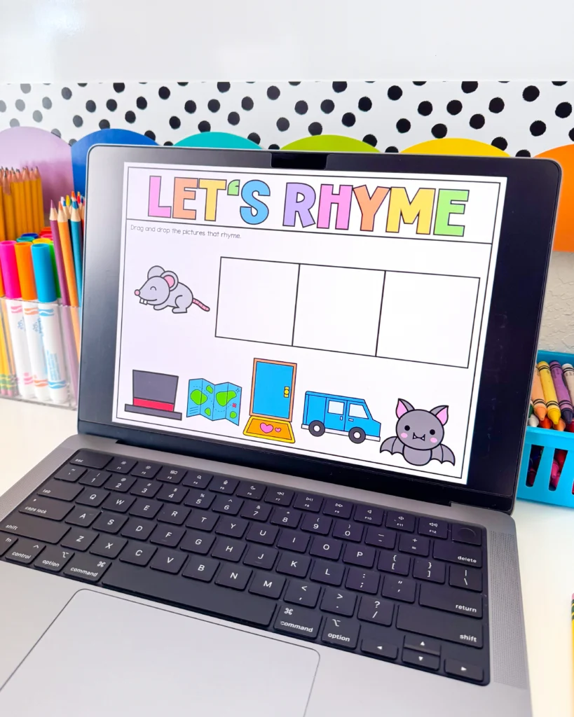 Laptop screen shows a children's rhyme worksheet titled "LET'S RHYME" with colorful letters and a drawing grid, surrounded by pencils and cartoon illustrations like a mouse and vehicle icons.