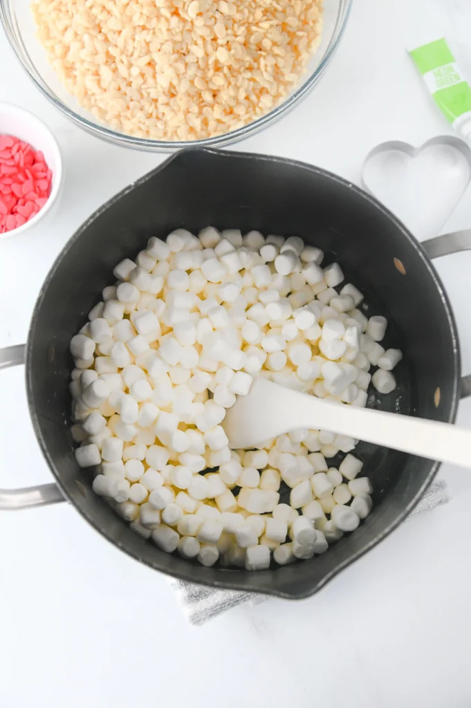 White mini marshmallows in a cooking pot with a spatula on a white surface.